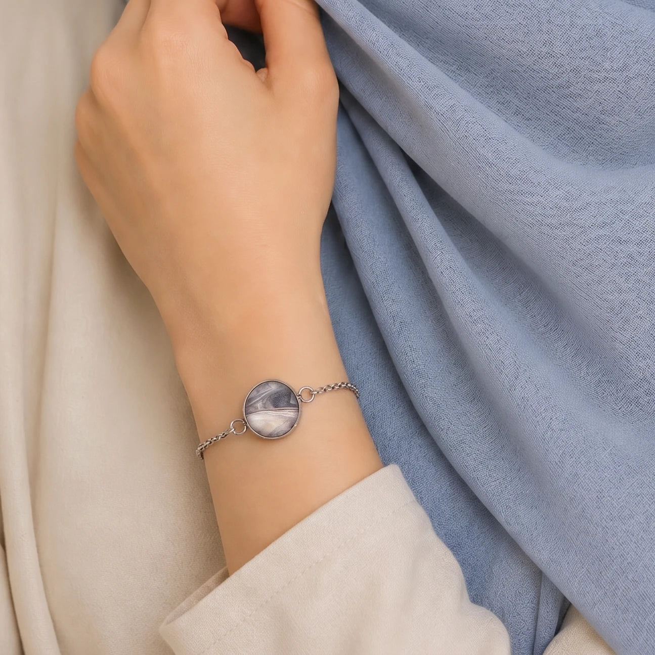 Model wearing Dar Suad stainless steel bracelet featuring marbling artwork in grey, silver, and beige.