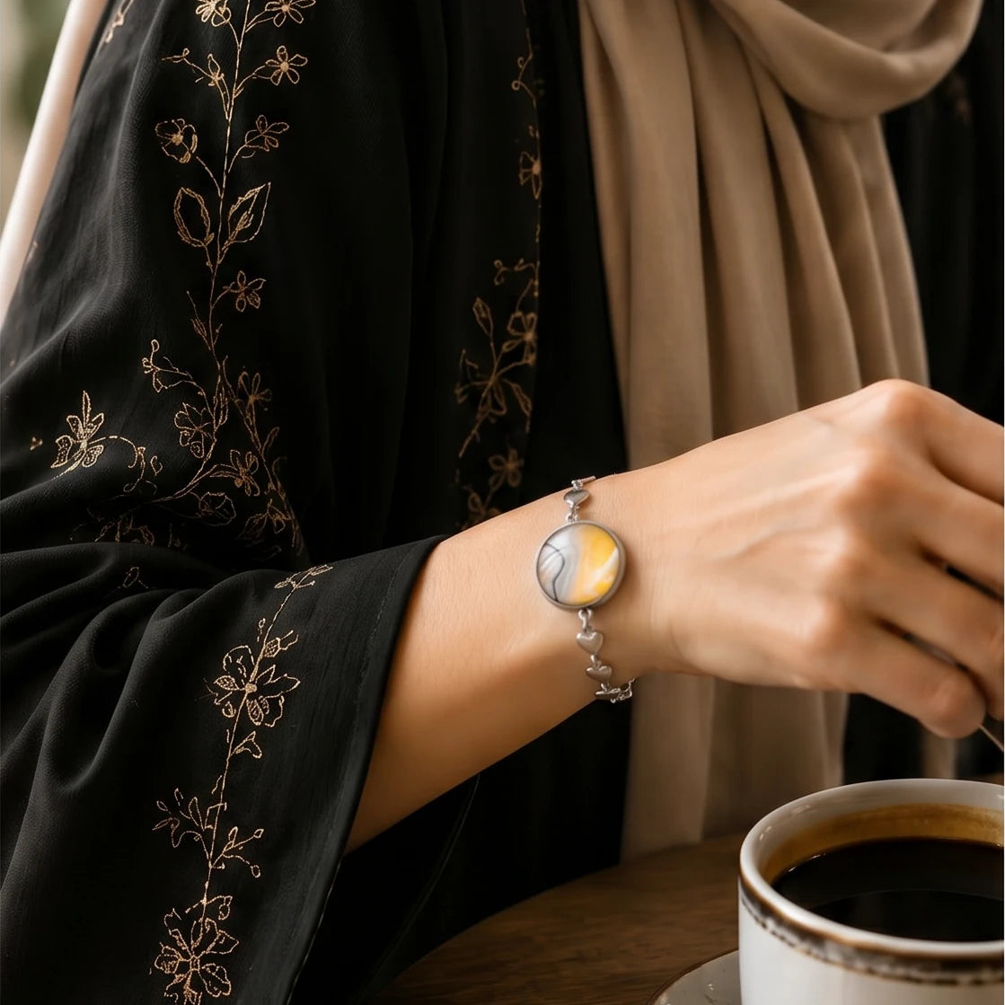 Model wearing Dar Suad stainless steel bracelet featuring marbling artwork in yellow, white, and grey.