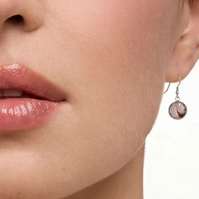 Model wearing Dar Suad stainless steel earrings featuring marbling artwork in grey, brown, and silver.