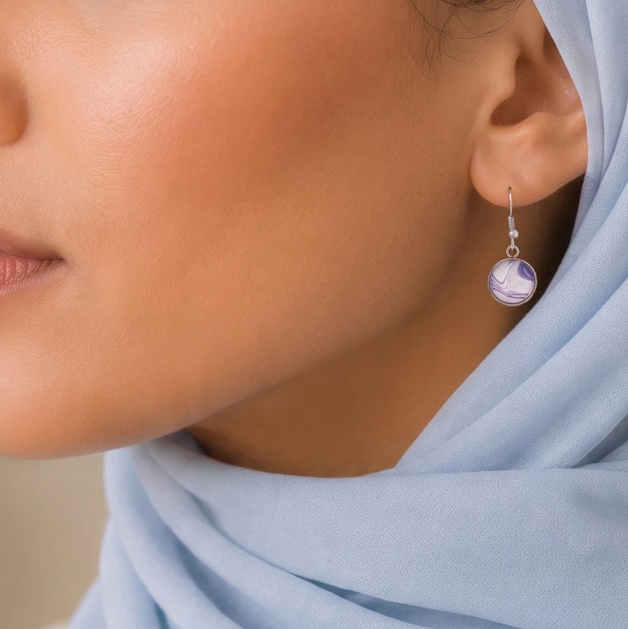 Model wearing Dar Suad stainless steel earrings featuring marbling artwork in purple and white.