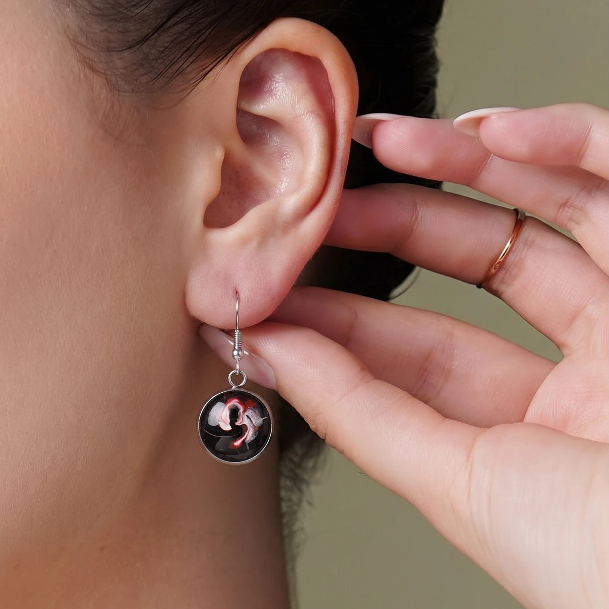 Model wearing Dar Suad stainless steel earrings featuring abstract artwork in black, red, and silver.