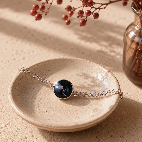 Dar Suad stainless steel abstract bracelet with a round black cabochon displayed in a handcrafted ceramic dish in warm natural sunlight.
