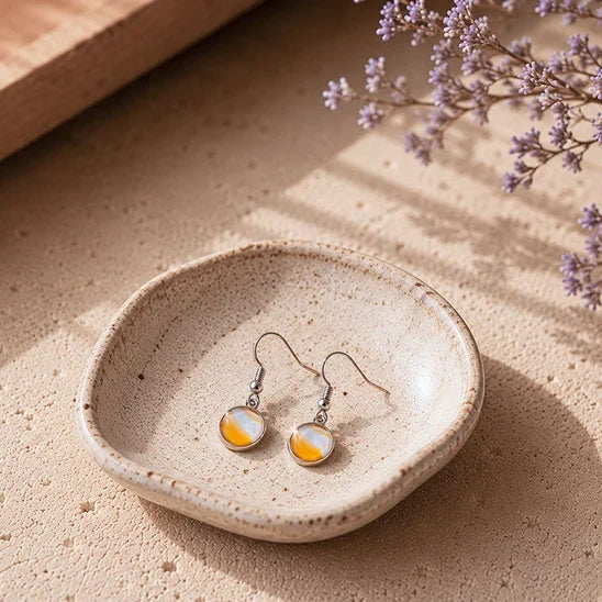 Dar Suad stainless steel round marbled earrings with yellow and white cabochons displayed in a handcrafted ceramic jewelry dish in warm natural sunlight.