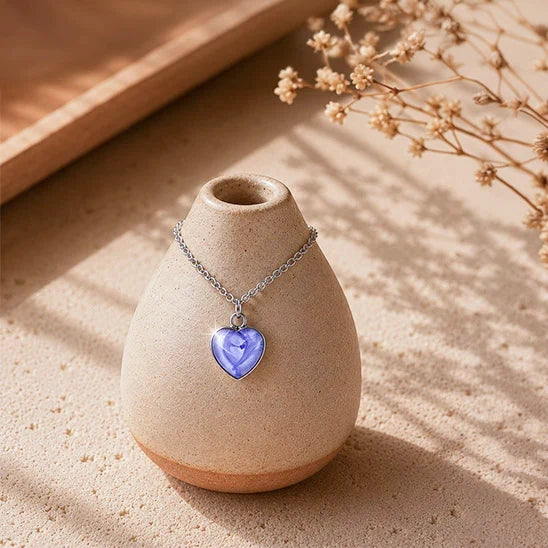 Dar Suad stainless steel heart marbled necklace with a purple cabochon displayed on a handcrafted ceramic vase in warm natural sunlight.