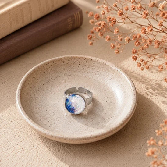 Dar Suad stainless steel hand-painted ring with a round blue and white cabochon displayed in a handcrafted ceramic dish in warm natural sunlight.