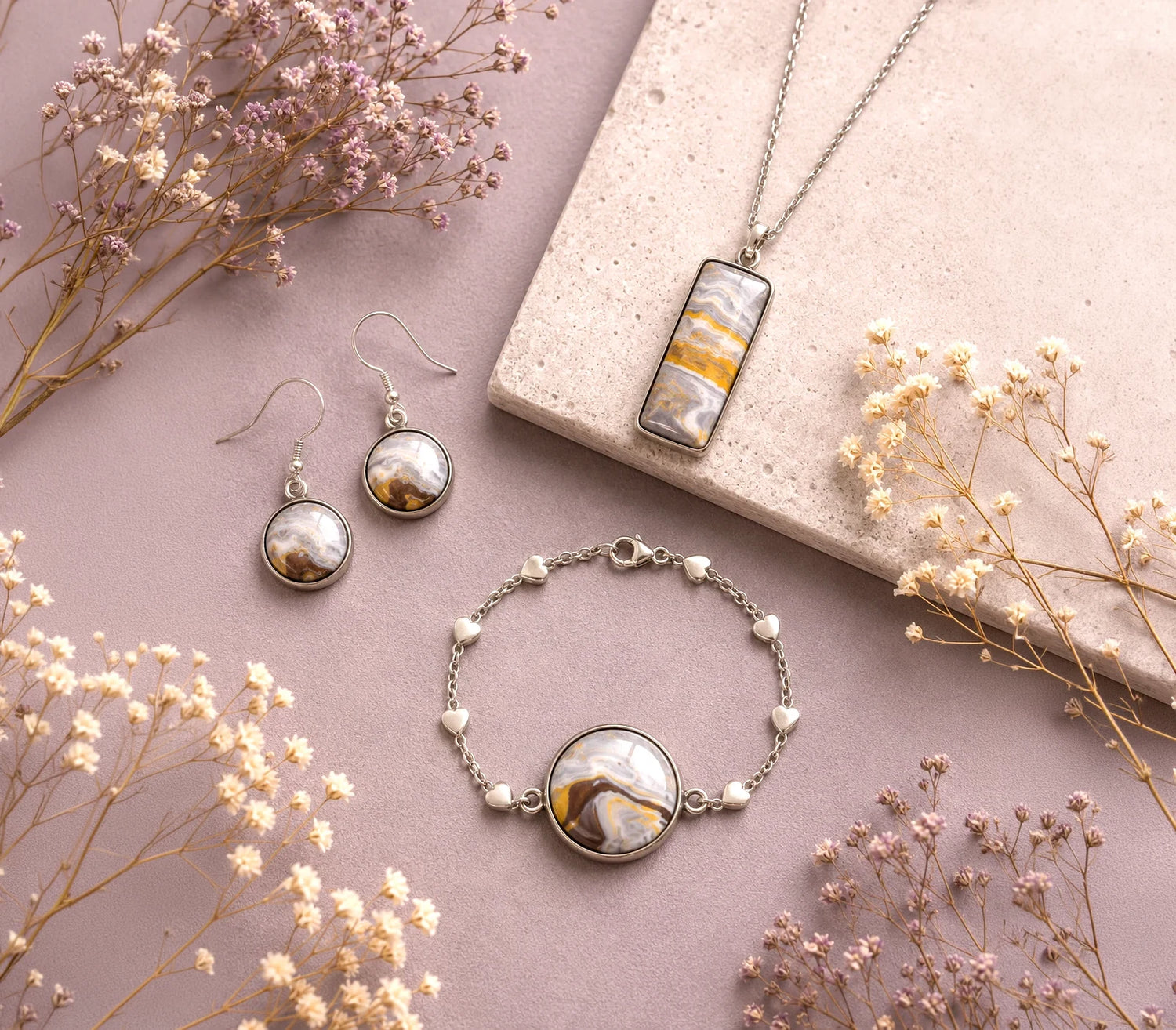 Jewelry set with desert-themed marbled necklace, earrings, and bracelet on a pink surface with dried flowers.