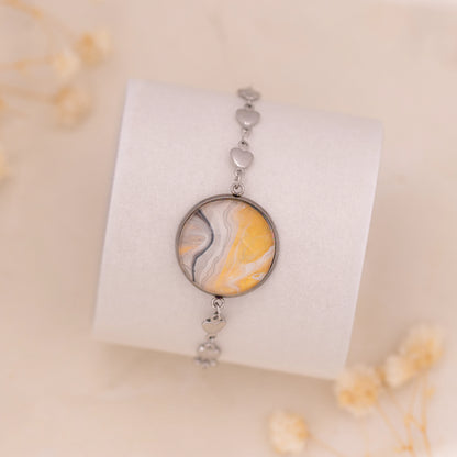 Dar Suad bracelet featuring marbling artwork in yellow, white, and grey with a stainless steel setting.