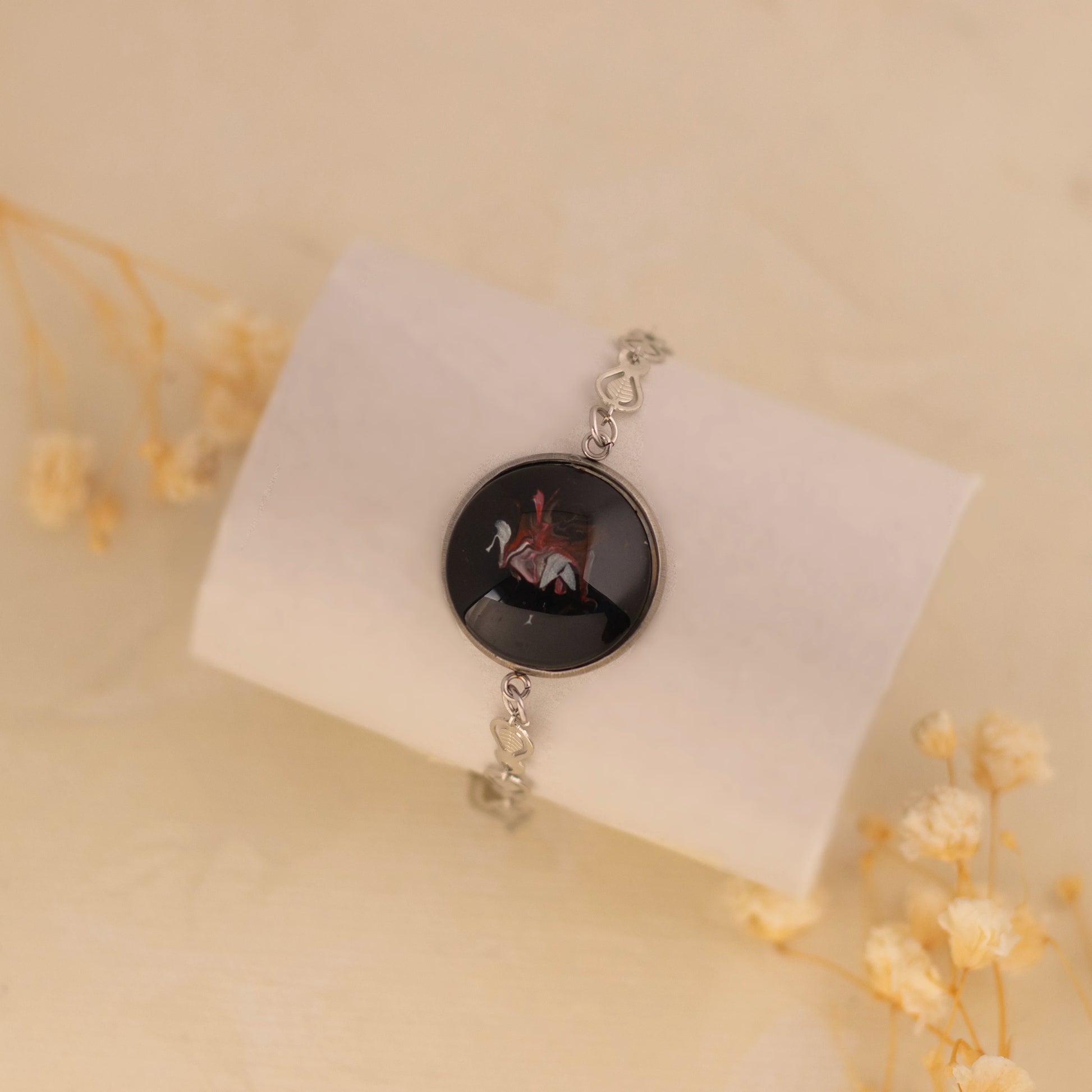 Dar Suad bracelet featuring one-of-a-kind original artwork in black, red, and silver with a stainless steel setting.
