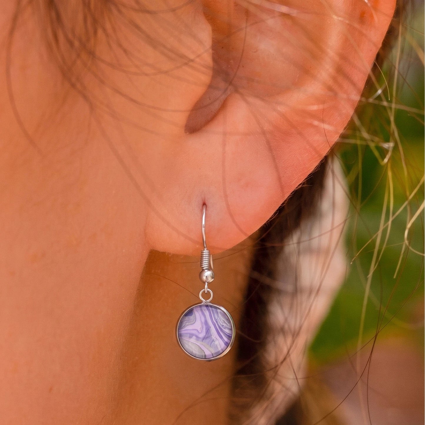 Model wearing Dar Suad stainless steel earrings featuring marbling artwork in purple and silver.