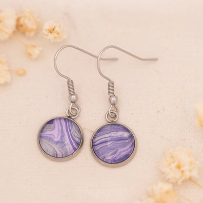 Dar Suad earrings featuring marbling artwork in purple and silver with a stainless steel setting.