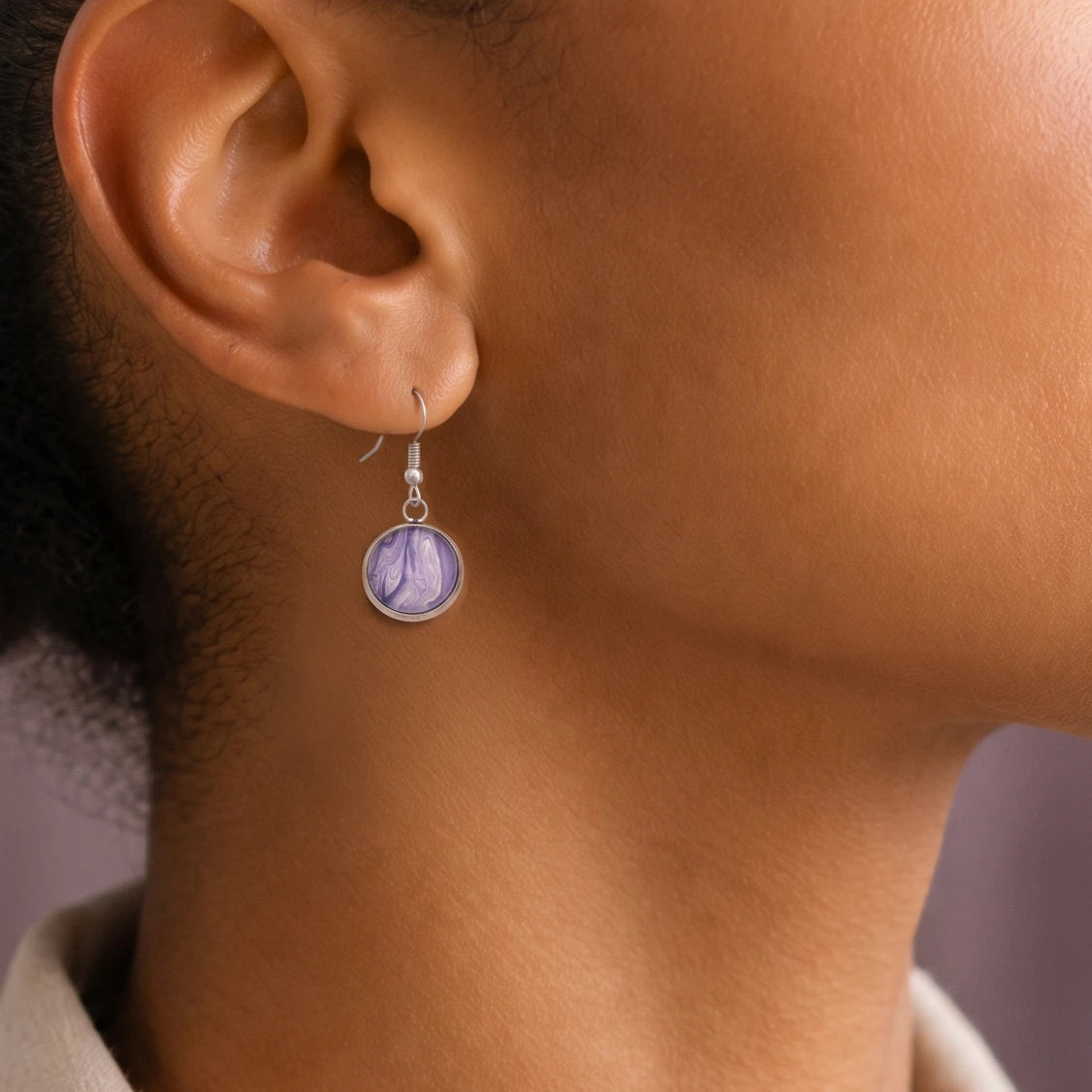 Model wearing Dar Suad stainless steel earrings featuring marbling artwork in purple and white.