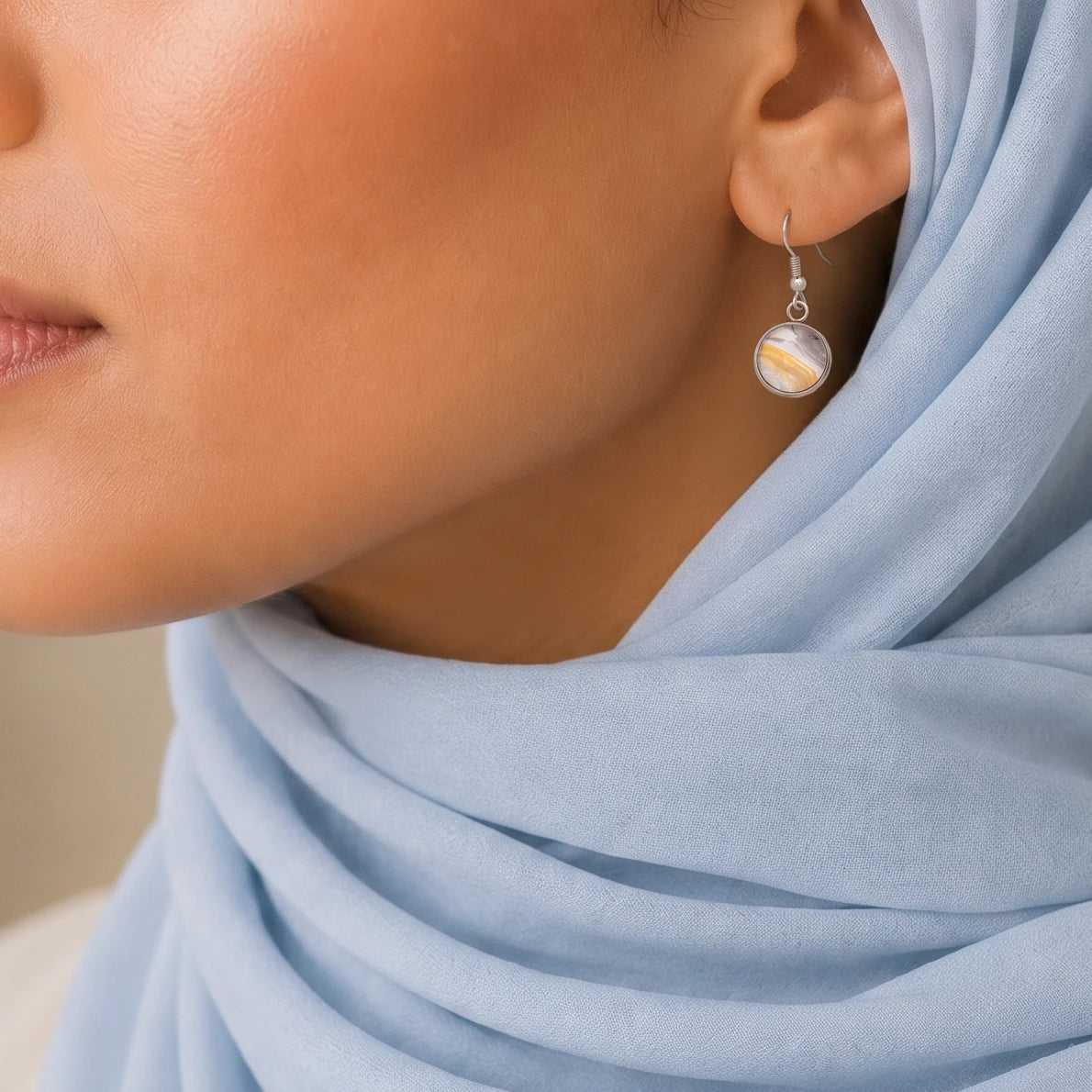 Model wearing Dar Suad stainless steel earrings featuring desert marbling artwork in grey, yellow, and white.