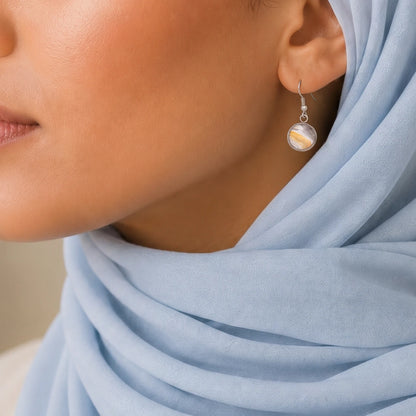 Model wearing Dar Suad stainless steel earrings featuring desert marbling artwork in grey, yellow, and white.
