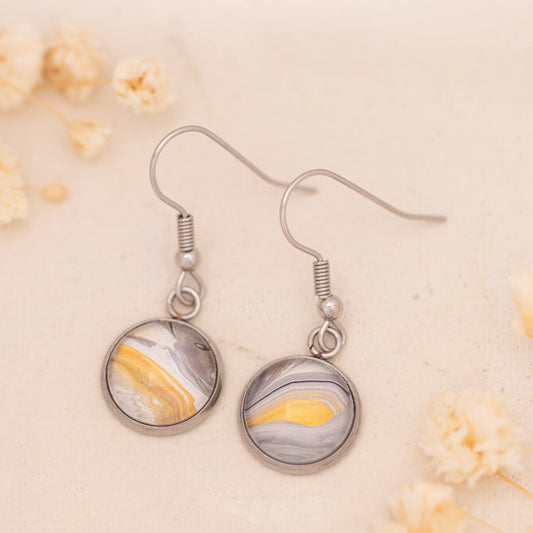 Dar Suad earrings featuring desert marbling artwork in grey, yellow, and white with a stainless steel setting.