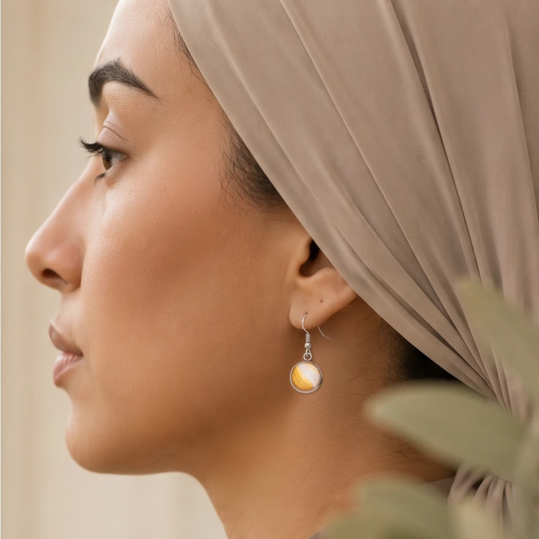 Model wearing Dar Suad stainless steel earrings featuring desert marbling artwork in yellow and white.