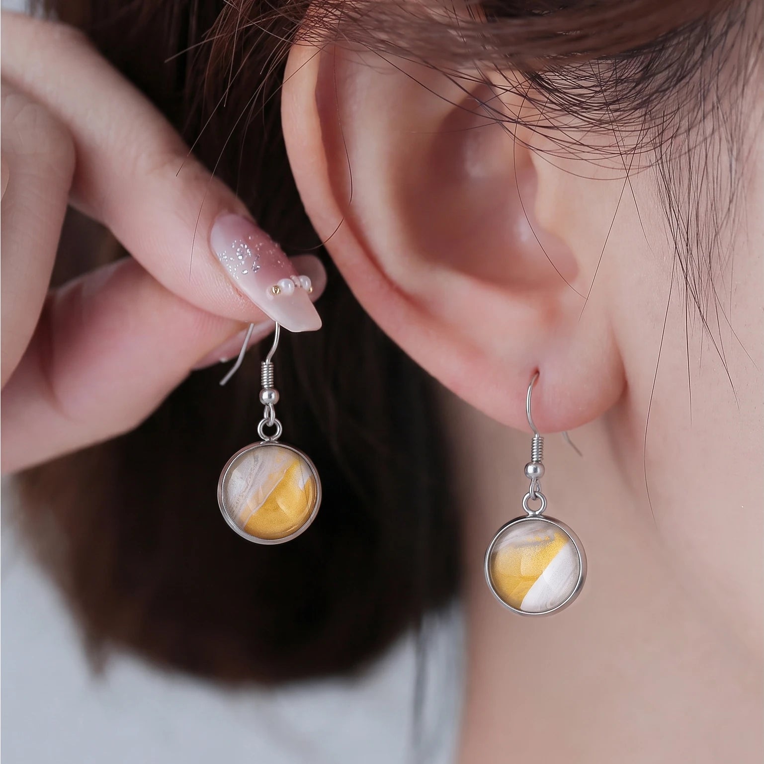 Model wearing Dar Suad stainless steel earrings featuring desert marbling artwork in yellow, grey, and white.