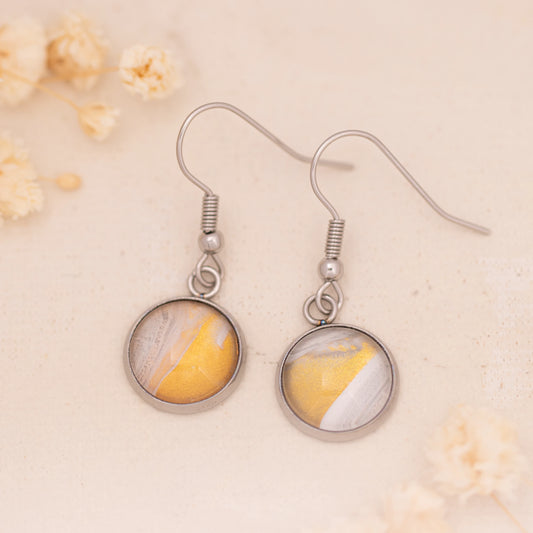 Dar Suad earrings featuring desert marbling artwork in yellow, grey, and white a stainless steel setting.