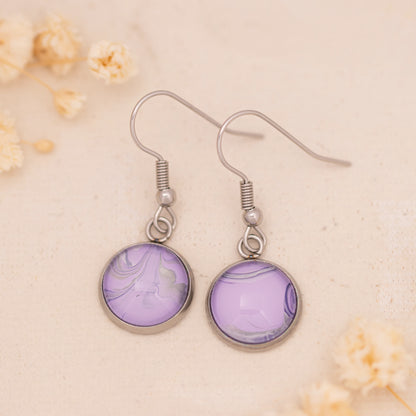 Dar Suad earrings featuring marbling artwork in purple and silver with a stainless steel setting.