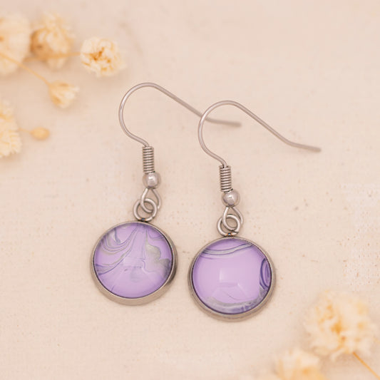 Dar Suad earrings featuring marbling artwork in purple and silver with a stainless steel setting.