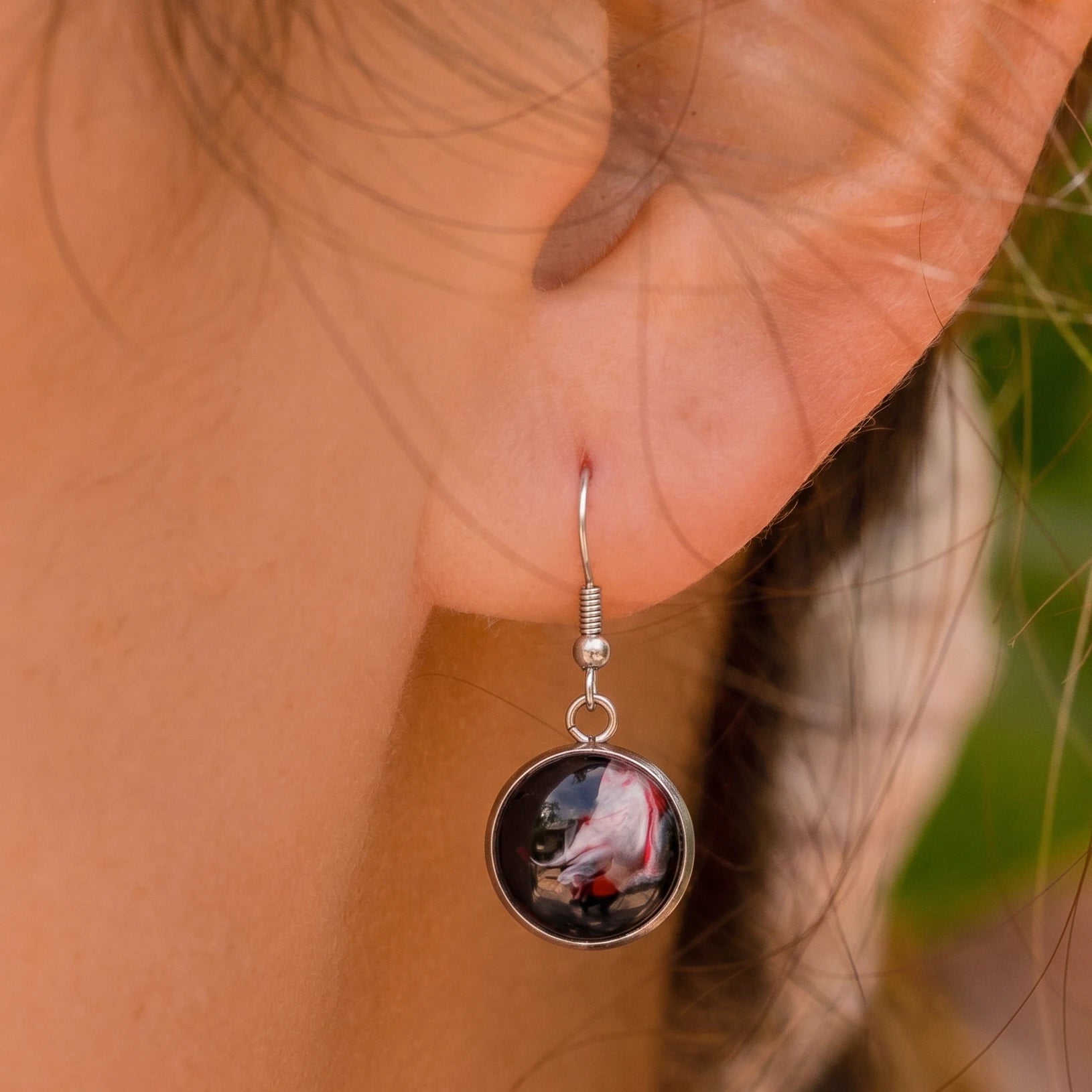 Model wearing Dar Suad stainless steel earrings featuring abstract artwork in black, red, and silver.