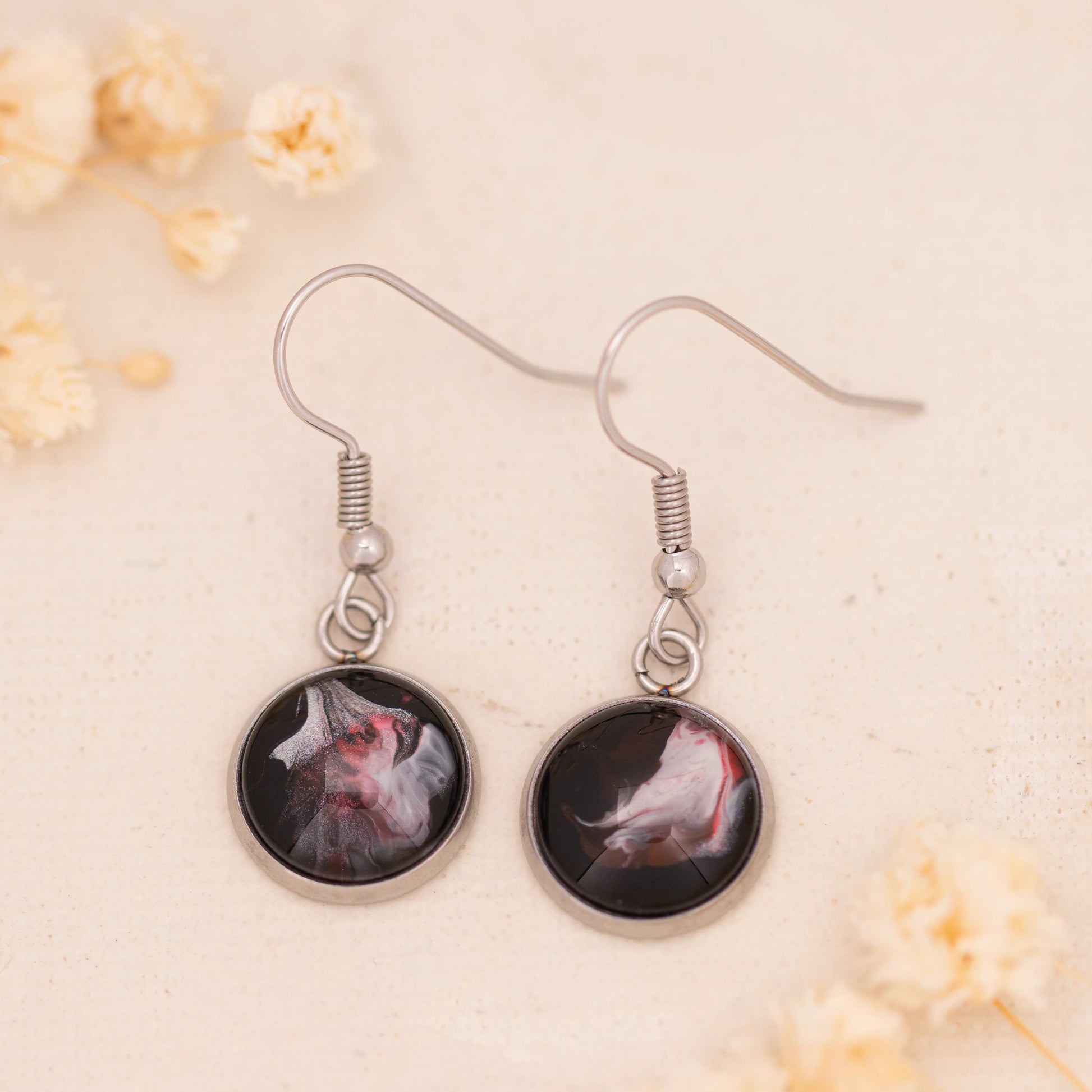 Dar Suad earrings featuring abstract artwork in black, red, and silver with a stainless steel setting.