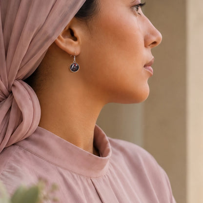 Model wearing Dar Suad stainless steel earrings featuring abstract artwork in black, red, and silver.