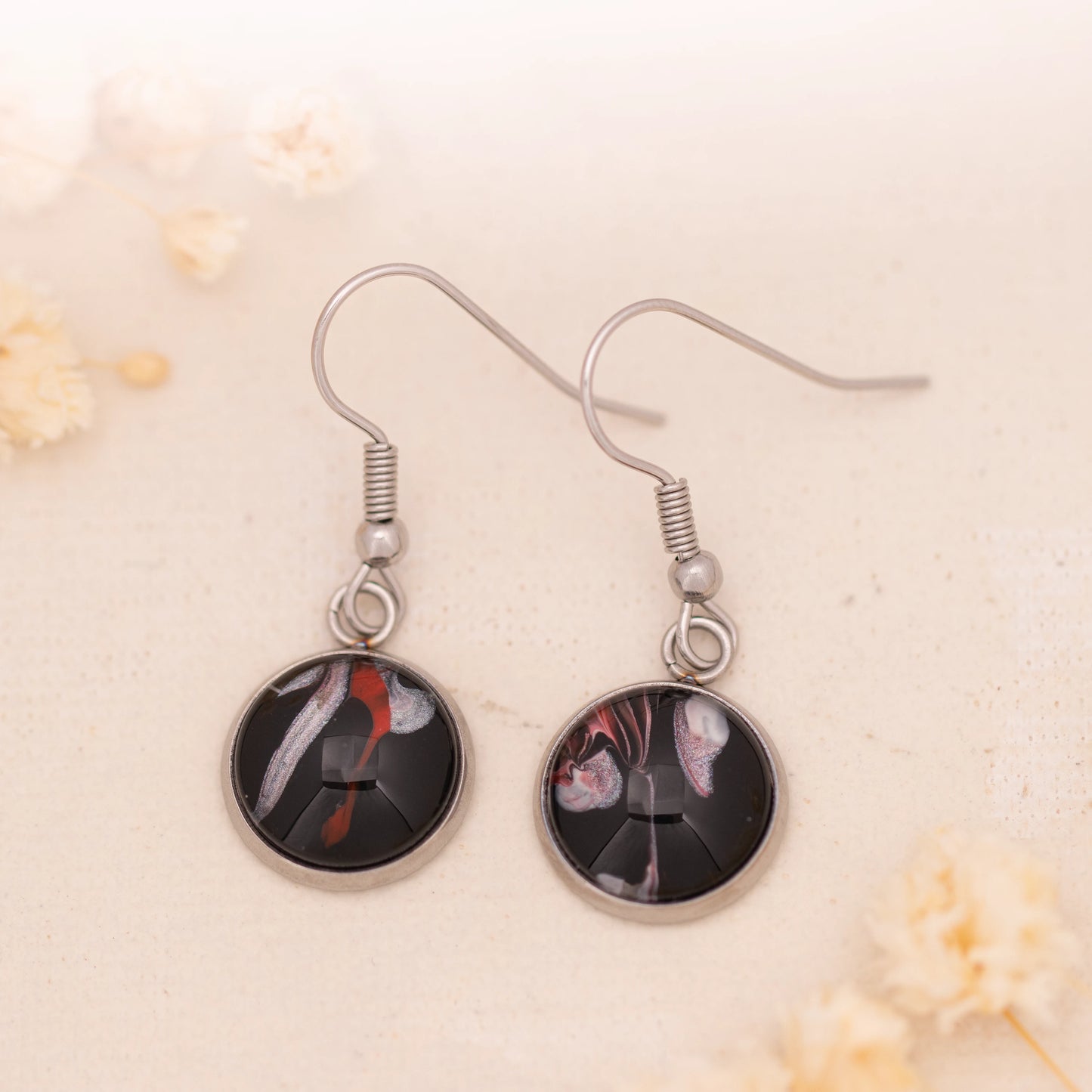 Dar Suad earrings featuring abstract artwork in black, red, and silver with a stainless steel setting.