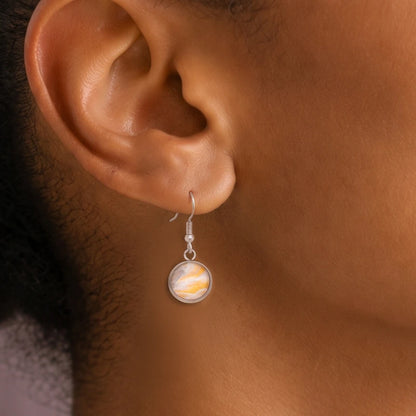 Model wearing Dar Suad stainless steel earrings featuring marbling artwork in yellow, white, and grey.