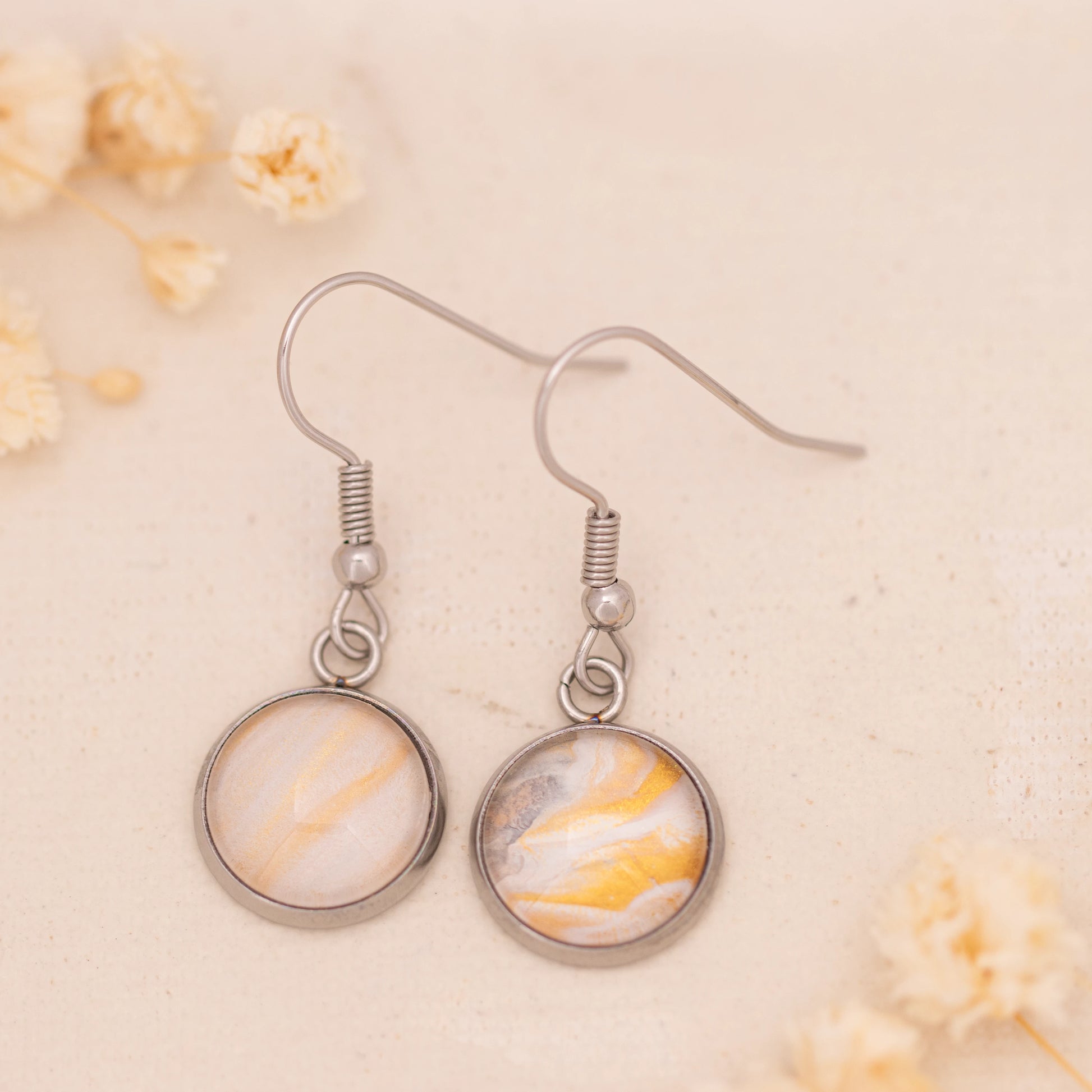 Dar Suad earrings featuring marbling artwork in yellow, white, and grey with a stainless steel setting.
