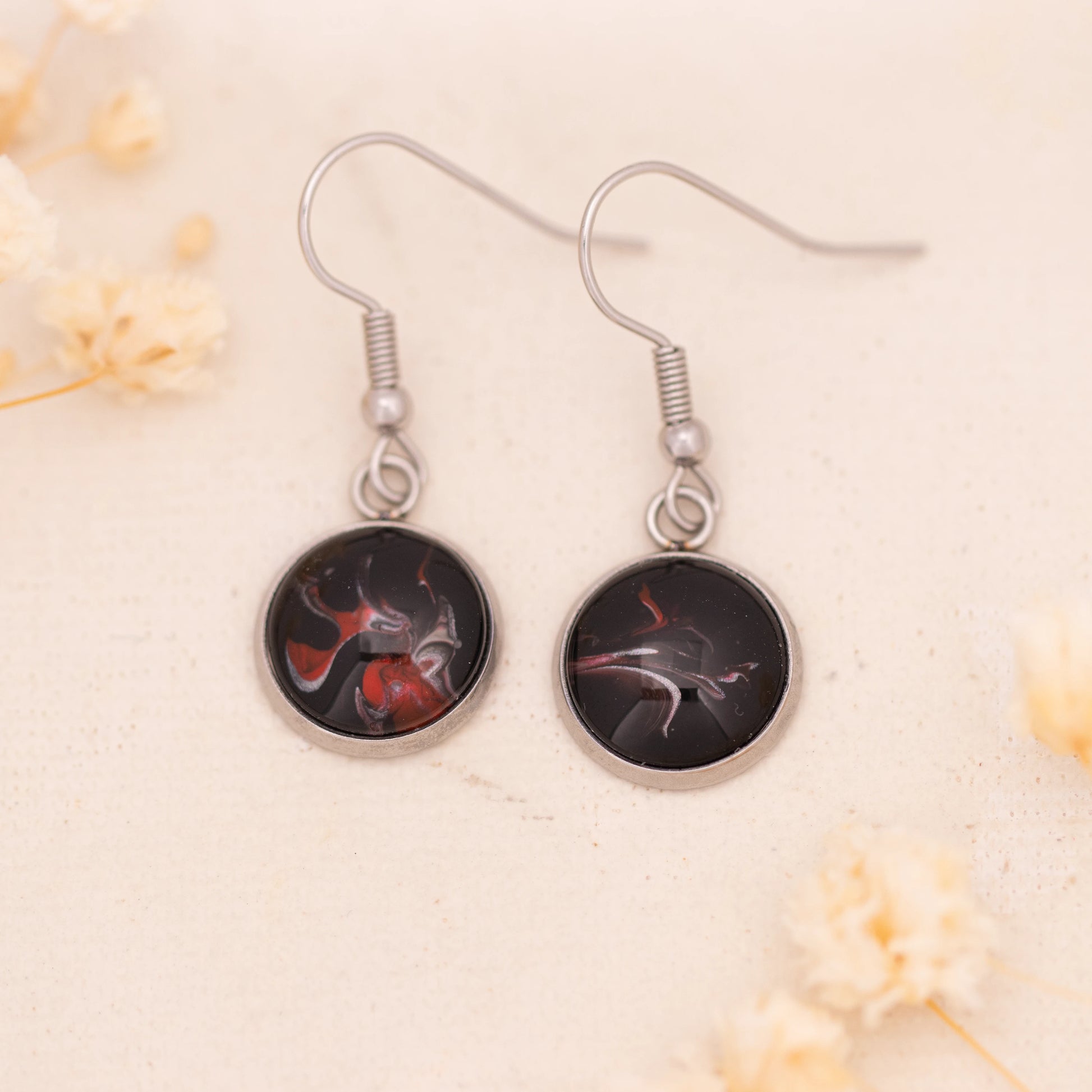 Dar Suad earrings featuring abstract artwork in black, red, and silver with a stainless steel setting.