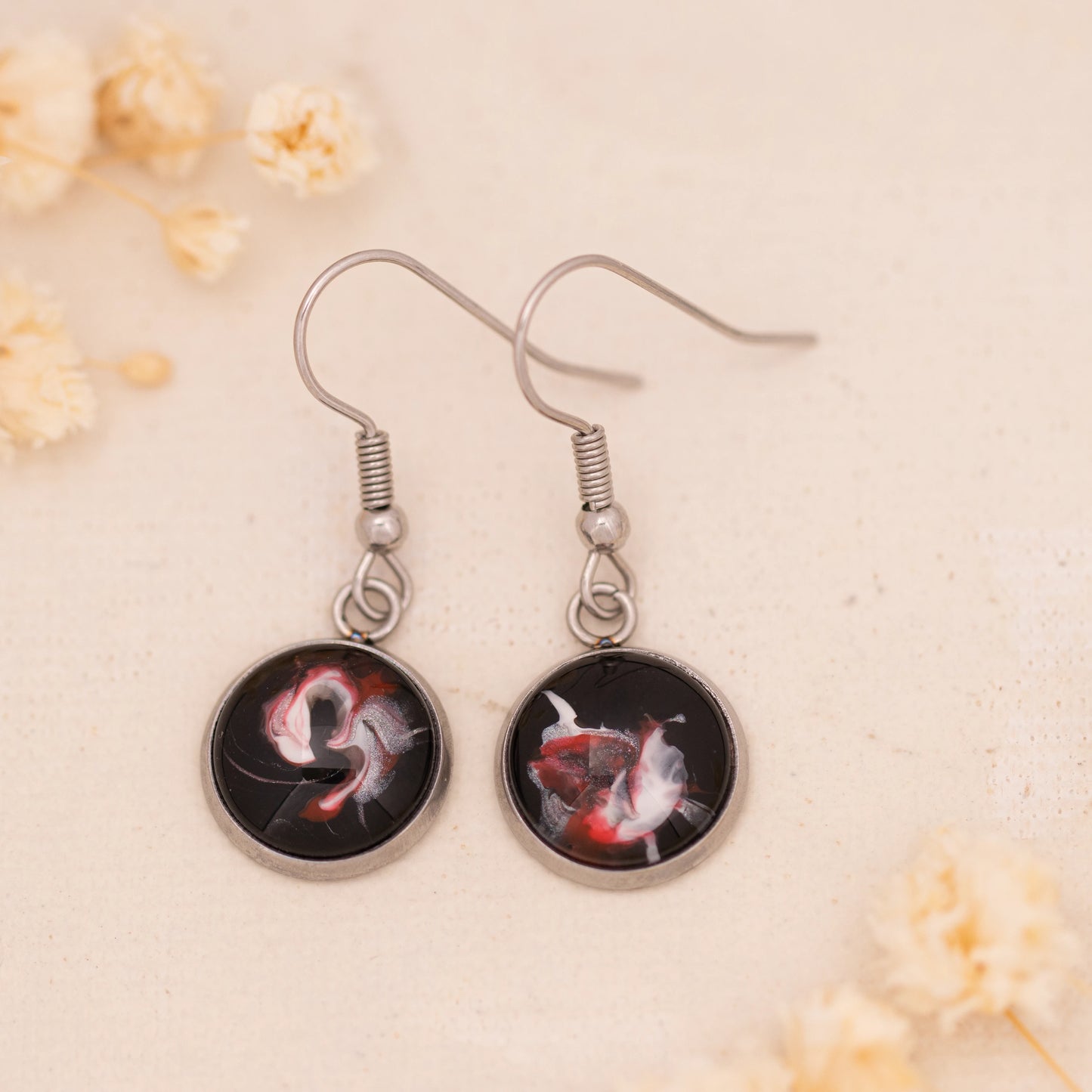 Dar Suad earrings featuring abstract artwork in black, red, and silver with a stainless steel setting.