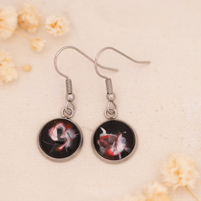 Dar Suad earrings featuring abstract artwork in black, red, and silver with a stainless steel setting.
