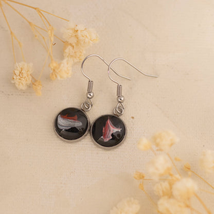 Dar Suad earrings featuring one-of-a-kind original artwork in black, red, and silver with a stainless steel setting.