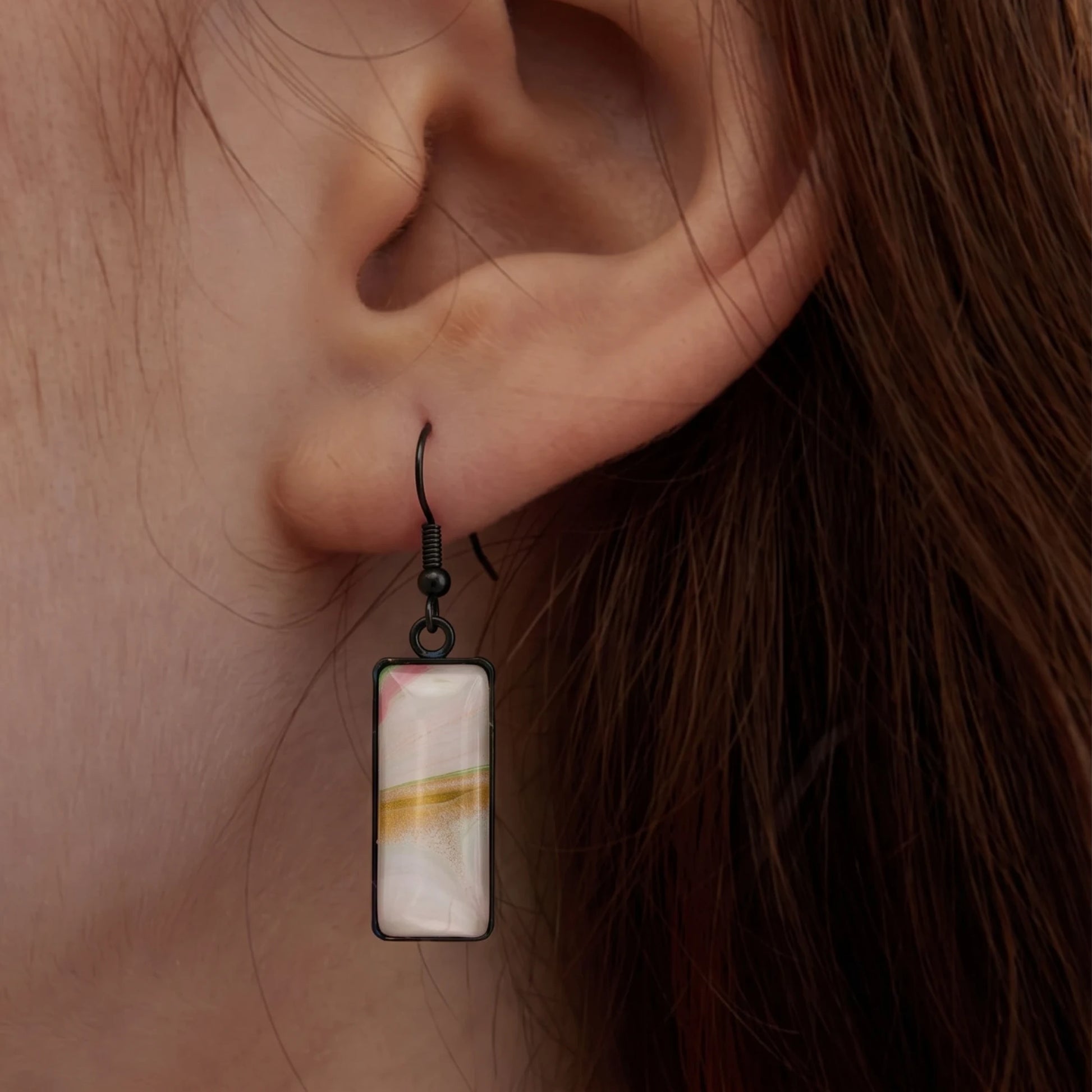 Model wearing Dar Suad stainless steel earrings featuring one-of-a-kind original artwork in white, gold, and pink.