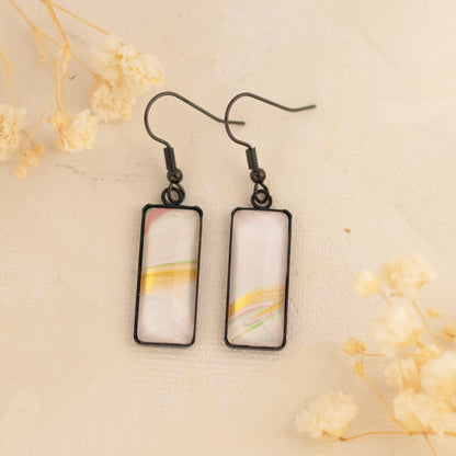 Dar Suad earrings featuring one-of-a-kind original artwork in white, gold, and pink with a stainless steel setting.