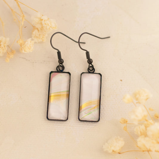 Dar Suad earrings featuring one-of-a-kind original artwork in white, gold, and pink with a stainless steel setting.