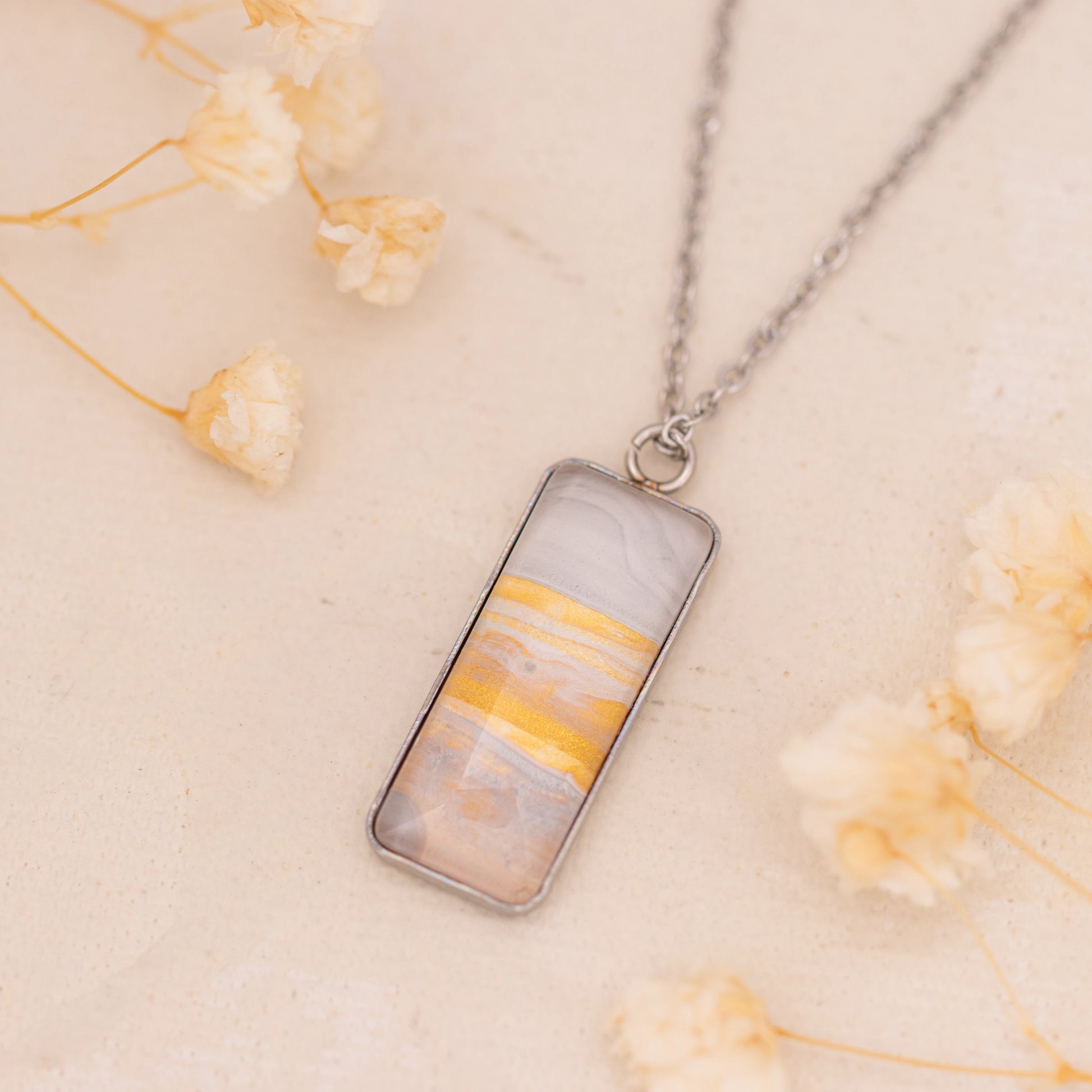 Dar Suad necklace featuring marbling artwork in white, yellow and grey with a stainless steel setting.