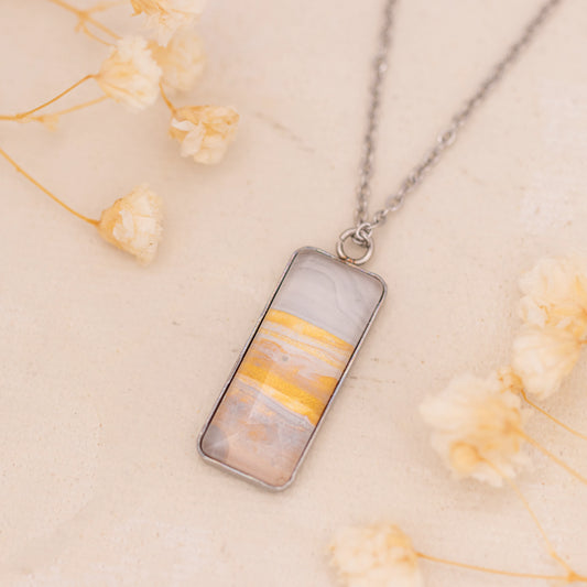 Dar Suad necklace featuring marbling artwork in white, yellow and grey with a stainless steel setting.