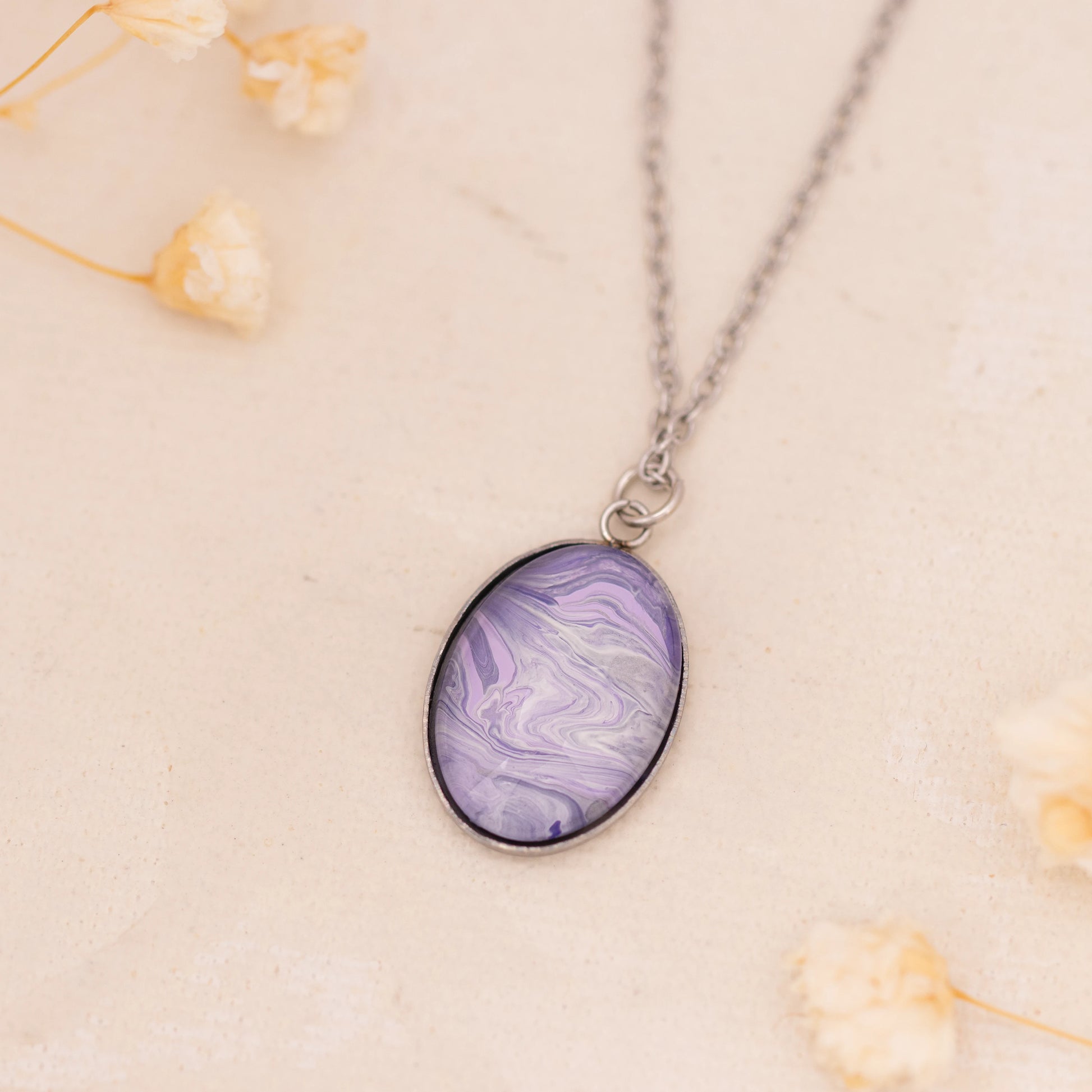 Dar Suad necklace featuring marbling artwork in purple and silver with a stainless steel setting.