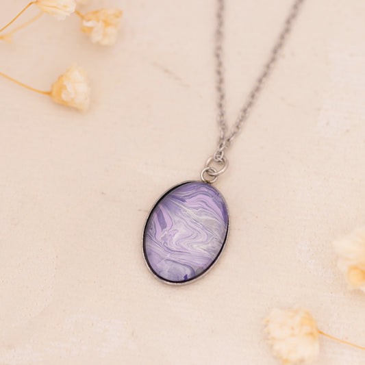 Dar Suad necklace featuring marbling artwork in purple and silver with a stainless steel setting.