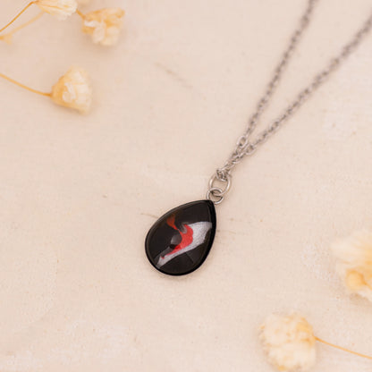 Dar Suad necklace featuring abstract artwork in black, red and silver with a stainless steel setting