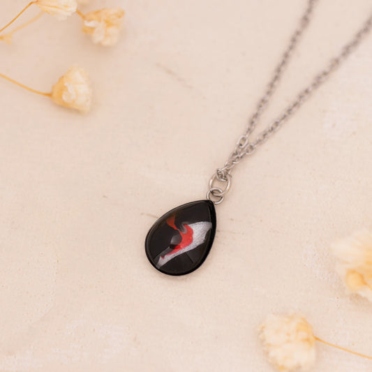 Dar Suad necklace featuring abstract artwork in black, red and silver with a stainless steel setting