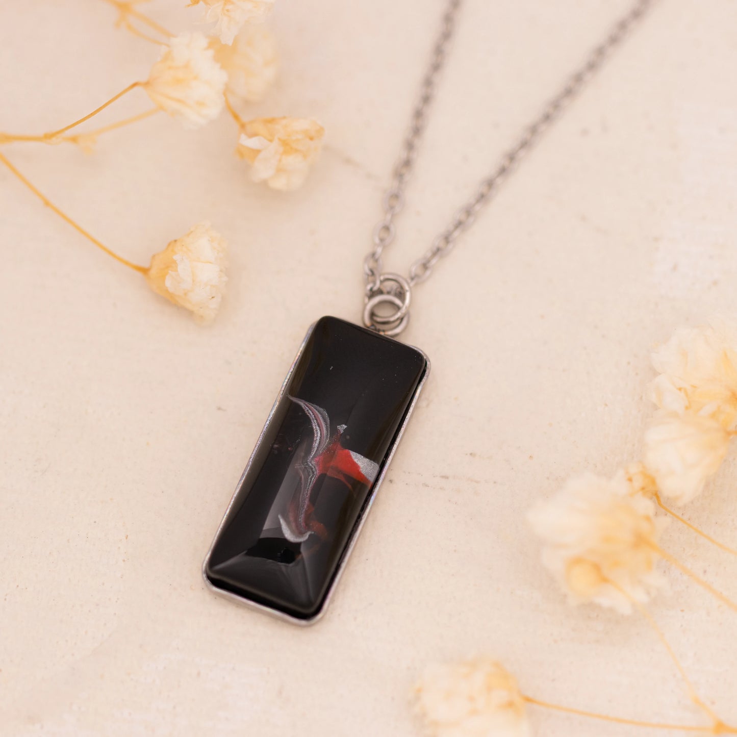 Dar Suad necklace featuring abstract artwork in black, red and silver with a stainless steel setting.
