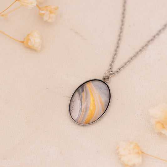 Dar Suad necklace featuring marbling artwork in white, yellow and grey with a stainless steel setting.