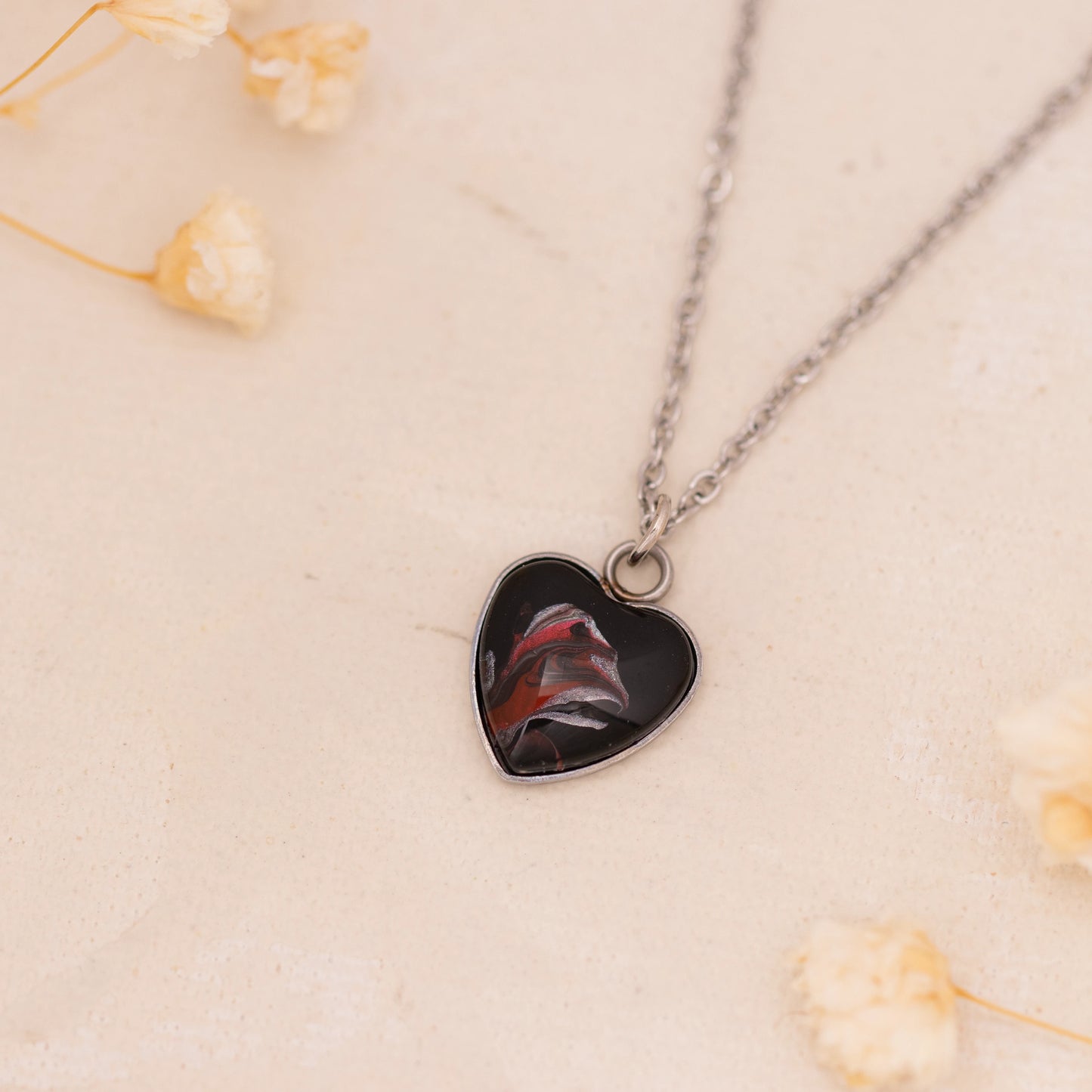 Dar Suad necklace featuring abstract artwork in black, red, and silver with a stainless steel setting.