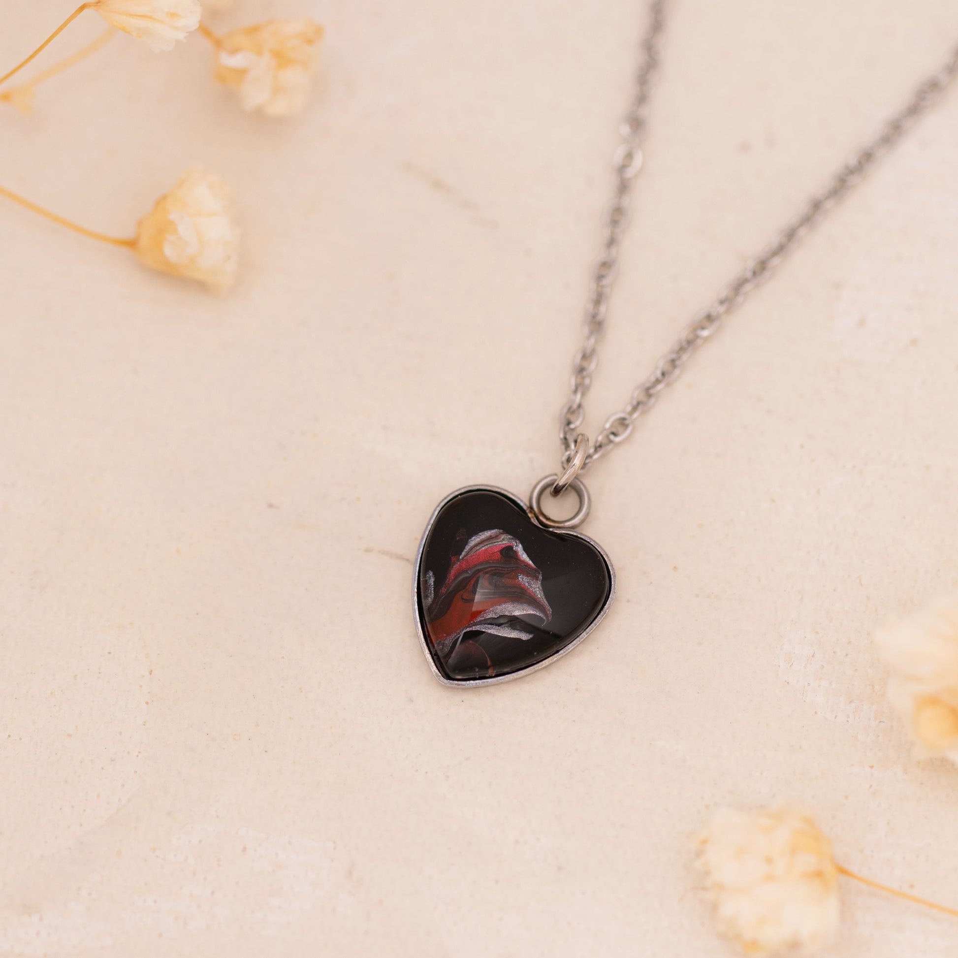 Dar Suad necklace featuring abstract artwork in black, red, and silver with a stainless steel setting.