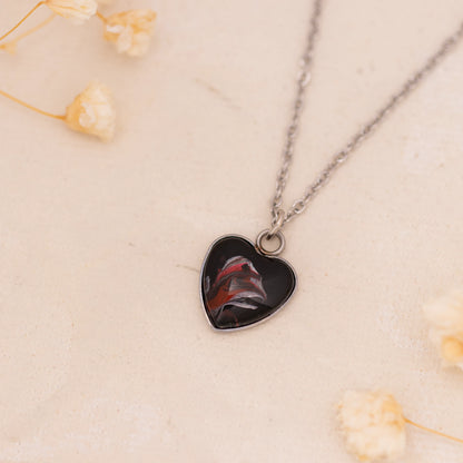 Dar Suad necklace featuring abstract artwork in black, red, and silver with a stainless steel setting.