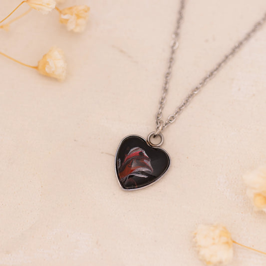 Dar Suad necklace featuring abstract artwork in black, red, and silver with a stainless steel setting.