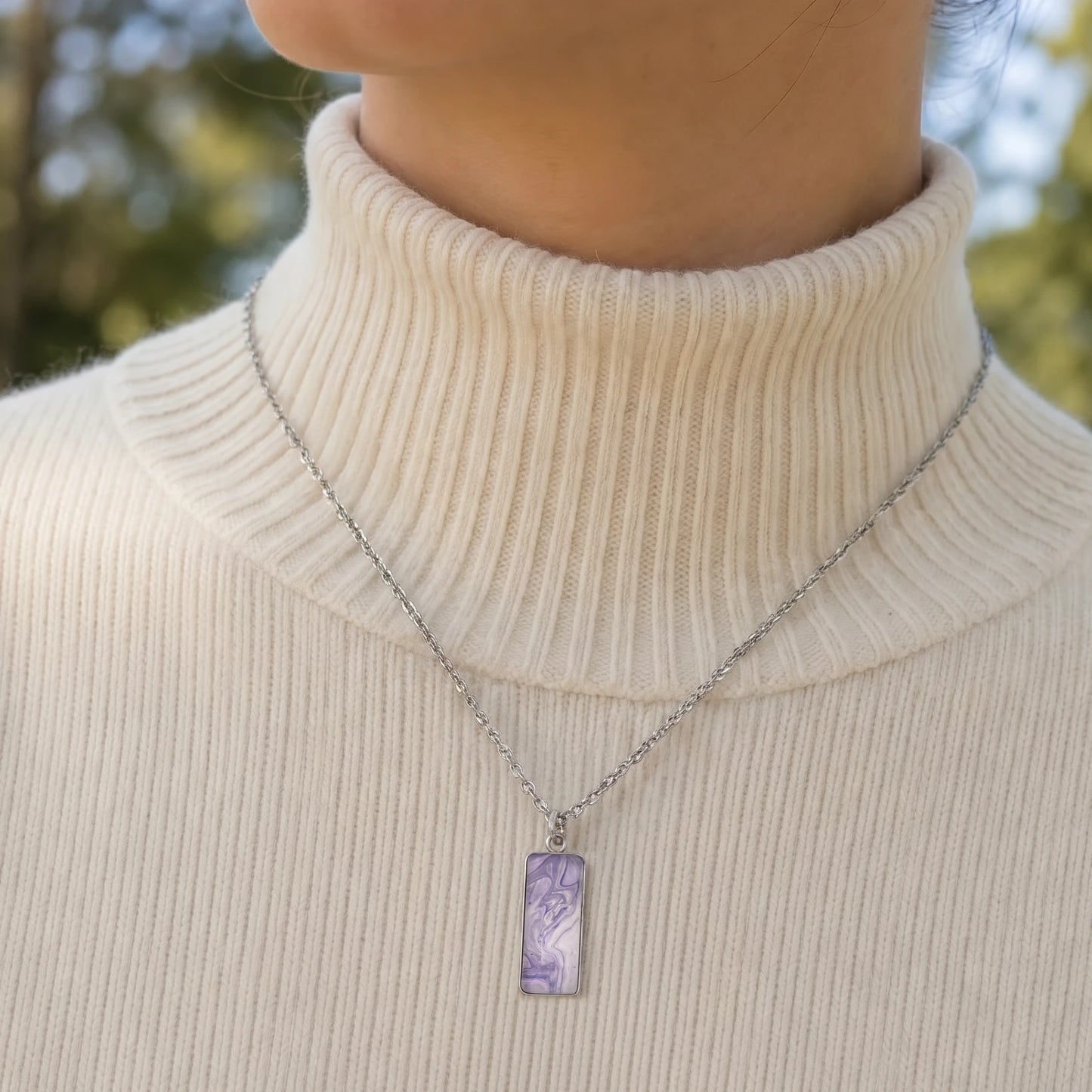 Model wearing Dar Suad stainless steel necklace featuring marbling artwork in purple and white.
