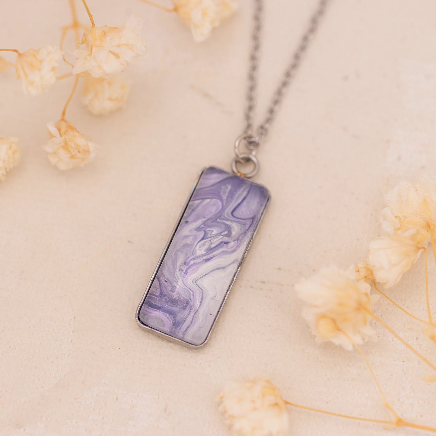 Dar Suad necklace featuring marbling artwork in purple and white with a stainless steel setting.